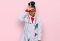 Young african american woman wearing doctor uniform and stethoscope making fun of people with fingers on forehead doing loser Royalty Free Stock Photo