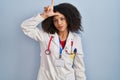 Young african american woman wearing doctor uniform and stethoscope making fun of people with fingers on forehead doing loser Royalty Free Stock Photo