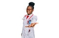 Young african american woman wearing doctor uniform and stethoscope smiling cheerful offering palm hand giving assistance and Royalty Free Stock Photo