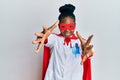 Young african american woman wearing doctor uniform and super hero costume looking at the camera smiling with open arms for hug Royalty Free Stock Photo