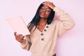 Young african american woman wearing glasses holding book stressed and frustrated with hand on head, surprised and angry face Royalty Free Stock Photo