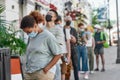 Young african american woman wearing mask waiting, standing in line with other people, respecting social distancing to