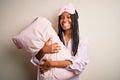 Young african american woman wearing pajama and eye mask hugging bed pillow with a happy face standing and smiling with a Royalty Free Stock Photo