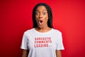 Young african american woman wearing sarcasm coments text on t-shirt over red background scared in shock with a surprise face,