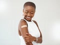 Young African American woman wearing and showing a bandaid on her arm standing against a white studio background. Happy