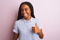 Young african american woman wearing striped shirt standing over isolated pink background doing happy thumbs up gesture with hand Royalty Free Stock Photo