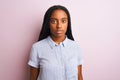 Young african american woman wearing striped shirt standing over isolated pink background with serious expression on face Royalty Free Stock Photo