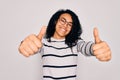 Young african american woman wearing striped sweater and glasses over white background approving doing positive gesture with hand, Royalty Free Stock Photo