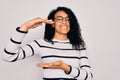 Young african american woman wearing striped sweater and glasses over white background gesturing with hands showing big and large Royalty Free Stock Photo