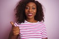 Young african american woman wearing striped t-shirt standing over isolated pink background doing happy thumbs up gesture with Royalty Free Stock Photo