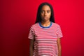 Young african american woman wearing striped t-shirt standing over isolated red background Relaxed with serious expression on face Royalty Free Stock Photo