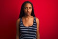 Young african american woman wearing striped t-shirt standing over isolated red background with serious expression on face Royalty Free Stock Photo