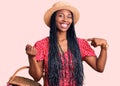 Young african american woman wearing summer hat and holding picnic wicker basket with bread pointing finger to one self smiling Royalty Free Stock Photo