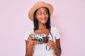 Young african american woman wearing summer hat holding vintage camera smiling looking to the side and staring away thinking Royalty Free Stock Photo