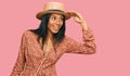 Young african american woman wearing summer hat very happy and smiling looking far away with hand over head Royalty Free Stock Photo