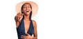 Young african american woman wearing swimsuit and summer hat laughing at you, pointing finger to the camera with hand over body, Royalty Free Stock Photo