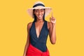 Young african american woman wearing swimsuit and summer hat showing and pointing up with finger number one while smiling Royalty Free Stock Photo