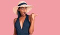 Young african american woman wearing swimsuit and summer hat surprised pointing with hand finger to the side, open mouth amazed Royalty Free Stock Photo