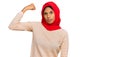 Young african american woman wearing traditional islamic hijab scarf strong person showing arm muscle, confident and proud of