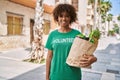 Young african american woman wearing volunteer t shirt holding groceries outdoors looking positive and happy standing and smiling Royalty Free Stock Photo