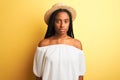 Young african american woman wearing white t-shirt and hat over isolated yellow background with serious expression on face Royalty Free Stock Photo