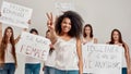 Young african american woman in white shirt showing peace sign, smiling at camera. Group of diverse women holding Royalty Free Stock Photo