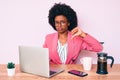 Young african american woman working at desk using computer laptop with angry face, negative sign showing dislike with thumbs Royalty Free Stock Photo