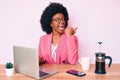 Young african american woman working at desk using computer laptop pointing thumb up to the side smiling happy with open mouth Royalty Free Stock Photo