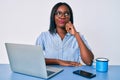 Young african american woman working at the office with laptop thinking concentrated about doubt with finger on chin and looking
