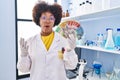 Young african american woman working at scientist laboratory holding money scared and amazed with open mouth for surprise, Royalty Free Stock Photo