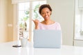 Young african american woman working using computer laptop smiling with happy face looking and pointing to the side with thumb up Royalty Free Stock Photo