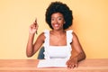 Young african american woman writing book surprised with an idea or question pointing finger with happy face, number one Royalty Free Stock Photo