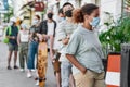 Young african american woman wearing mask waiting, standing in line with other people, respecting social distancing to