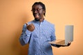 Young african american worker man working using laptop standing over yellow background pointing and showing with thumb up to the Royalty Free Stock Photo