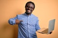 Young african american worker man working using laptop standing over yellow background with surprise face pointing finger to Royalty Free Stock Photo