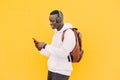 Young african black man against a yellow wall wearing a white sweatshirt and a backpack listening music on wireless headphones whi Royalty Free Stock Photo