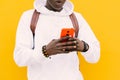 Young african black man against a yellow wall wearing a white sweatshirt and a backpack listening music on wireless headphones whi Royalty Free Stock Photo