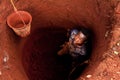 Young african boy inside water well in africa during digging looking in camera seen from above, with bucket going down