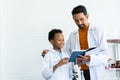 Young African boy in a white lab coat learns about an experimental error in blue textbook after a teacher teaches Royalty Free Stock Photo