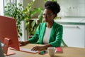 Young African businesswoman in eyeglasses and formal wear working remotely in cozy home kitchen