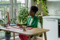 Young African businesswoman in eyeglasses and formal wear working remotely in cozy home kitchen