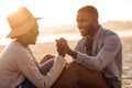 Young African couple sitting together on a beach at sunset
