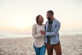 Young African couple walking on a beach at sunset laughing Royalty Free Stock Photo