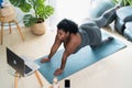 Young African curvy woman doing pilates virtual fitness class with laptop at home Royalty Free Stock Photo