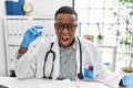 Young african doctor man holding syringe at the hospital angry and mad screaming frustrated and furious, shouting with anger Royalty Free Stock Photo