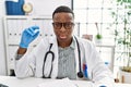 Young african doctor man holding syringe at the hospital looking sleepy and tired, exhausted for fatigue and hangover, lazy eyes