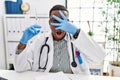 Young african doctor man holding syringe at the hospital peeking in shock covering face and eyes with hand, looking through