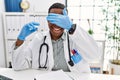 Young african doctor man holding syringe at the hospital smiling and laughing with hand on face covering eyes for surprise