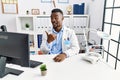 Young african doctor man wearing stethoscope at the clinic smiling with happy face looking and pointing to the side with thumb up Royalty Free Stock Photo