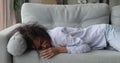 African woman feels tired falls down on sofa at home
